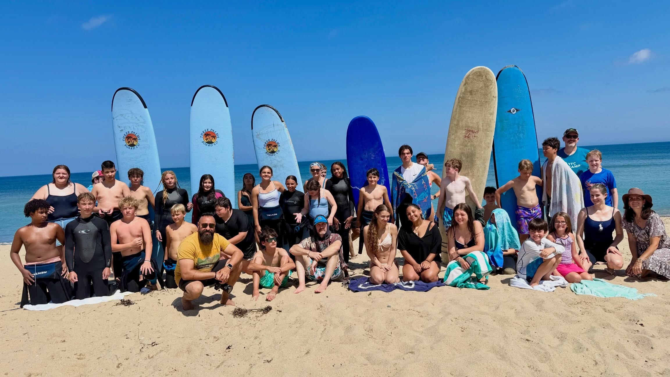 YFC Cape Cod students and leaders gathered on the beach with surfboards